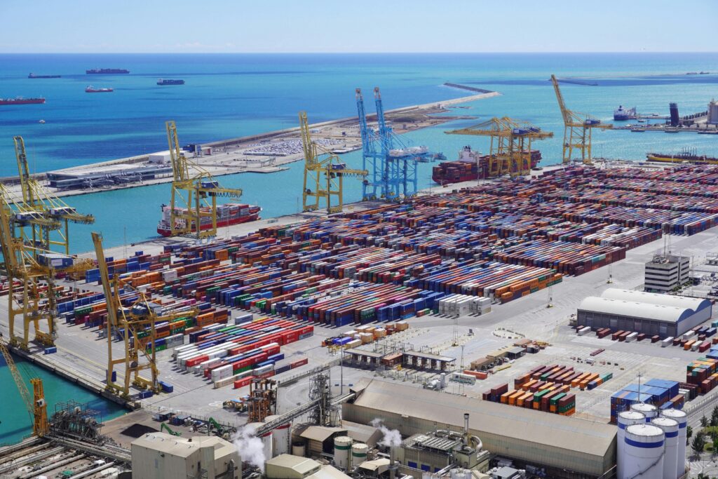 Dynamic aerial view of shipping containers and cranes in Barcelona port handling logistics.